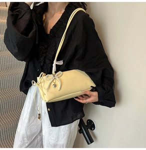 Detail view of yellow shoulder bag with pearl bow, heart tag and lace strap