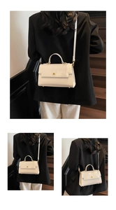 Close-up of white glossy leather crossbody bag with gold hardware on a black blazer