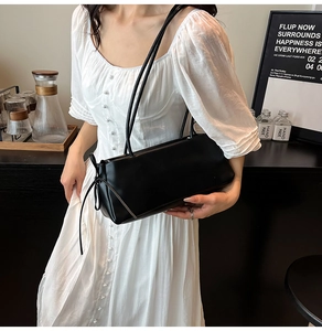 Detail of a black leather underarm bag with long shoulder straps on a white dress