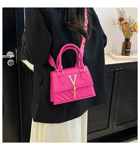 Gros plan du sac fuchsia avec logo V doré, gland métallique et bandoulière tissée