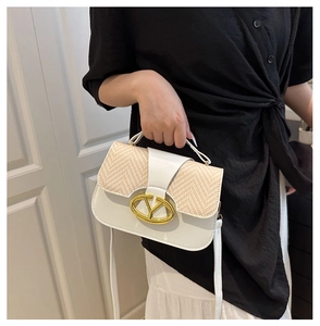 Close-up of a white leather and straw saddle bag with a gold buckle worn by a model
