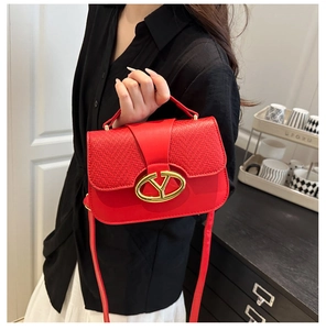 Detail of red saddle bag featuring woven texture flap and golden oval buckle