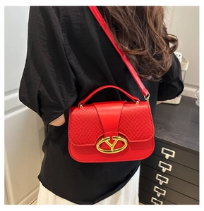 Detail of red crossbody bag with textured fabric flap and gold V-shaped metal buckle