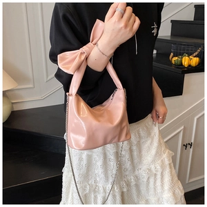 Pink patent leather handbag with a large bow detail and thin metal chain strap on model