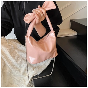 Macro detail of glossy pink patent leather bag featuring a bow handle and silver chain