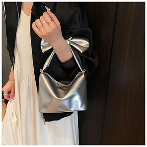 Detail shot of a silver bow handbag styled with a white dress and black jacket
