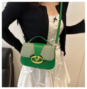 Detail of green saddle bag with woven pattern flap and golden metal V-shaped logo buckle