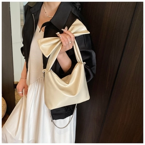 Detail showing creamy bow handbag with glossy finish and elegant metal chain strap