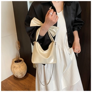 Detail of a creamy white patent leather bow handbag with a metallic chain strap on a model