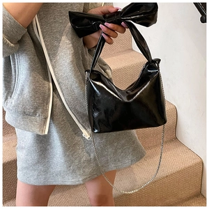 Close-up of black patent leather bag featuring a bow handle and silver chain strap details