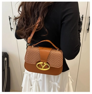 Close-up of saddle bag featuring brown herringbone fabric and oval gold buckle detail