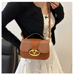 Detail of a brown leather saddle bag with woven texture and gold letter buckle