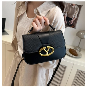 Close-up of golden V-shaped buckle and textured flap on black leather handbag