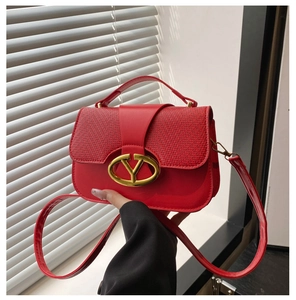 Close-up of bright red saddle bag with woven texture and gold V-shaped metal logo
