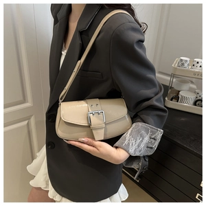 Detail of a chic cream underarm bag with a silver square buckle on a model shoulder