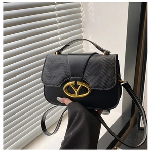 Detail of black saddle bag featuring woven texture flap and gold oval metal buckle