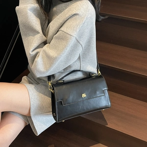 Classic black faux leather crossbody bag with gold hardware and top handle shown on model