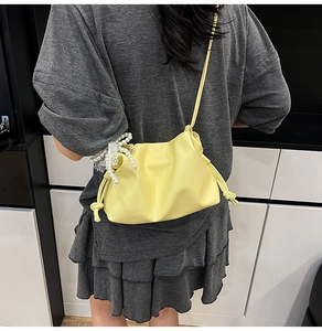 Detail of soft yellow pleated bucket bag featuring pearl and lace charms for women