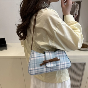 Chic plaid underarm bag with decorative bow and slim leather strap shown on a model