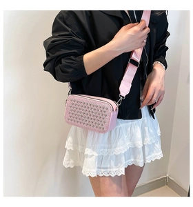 Pink rectangular crossbody bag with silver studs and a wide nylon strap on a fashion model