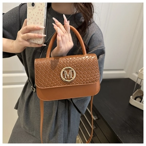 Détail d'un sac à main marron tressé avec logo 'M' doré tenu par un mannequin