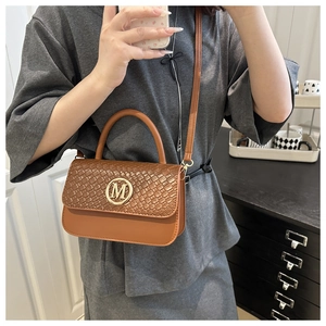 Detail of a brown crossbody bag featuring a woven flap and a gold metallic M buckle