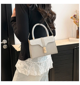 Detail showing glittery silver top handle and gold lock on grey faux leather crossbody bag