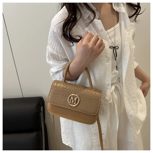 Détail d'un sac bandoulière marron avec boucle M dorée et texture croco sur un tailleur