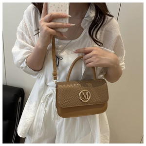 Detail of light brown leather handbag featuring woven flap and gold metal M-logo buckle