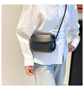 Model wearing a minimalist black leather saddle bag with smooth flap closure