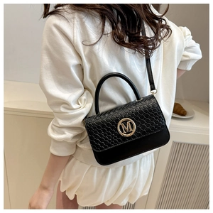 Close-up of black crossbody bag featuring woven texture and golden letter M logo