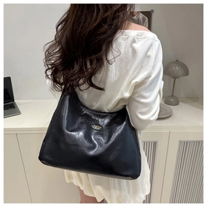 Macro detail of glossy black hobo bag with gold metal plaque shown in modern office setting