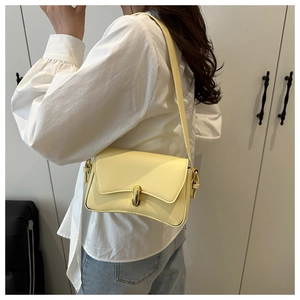Detail view of pale yellow shoulder bag with curved base and golden metallic turn-lock