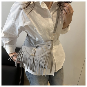 Macro detail of grey fringe crossbody bag with gold metal buckle and boho tassels