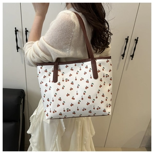 Détail du sac cabas à imprimé cerise rouge et anses marron porté par un mannequin