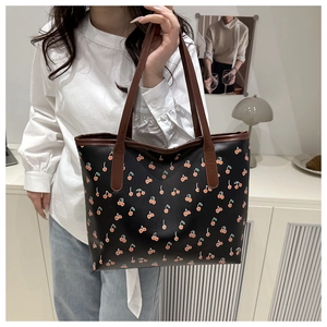 Detail of floral tote bag featuring red cherry prints and brown leather straps