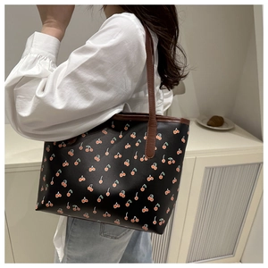 Detail of black tote bag with red cherry print and slim brown handles on model shoulder