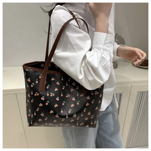 Close-up of black tote bag with cherry print and contrast brown faux leather straps