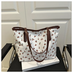 Close-up of a large floral tote bag with red cherry prints and brown leather trim detailing