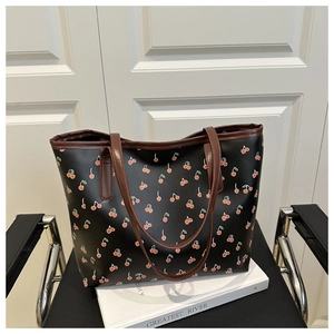 Close-up of a black tote bag with red cherry prints and brown PU leather shoulder straps