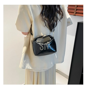 Détail d'un sac cabas noir brillant orné d'un logo S en clous argentés sur le devant