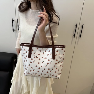 White tote bag with red cherry print and brown handles, shown held by a model in a room