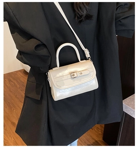 Detail of cream white patent leather small square bag with metal buckle on black suit