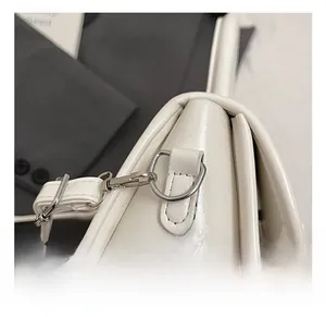 Detail of premium silver D-ring hardware on a cream patent leather crossbody bag