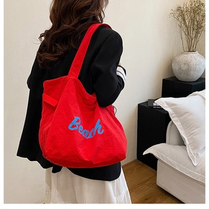 Detailed back view of a large red canvas tote bag with blue Beach embroidery on model