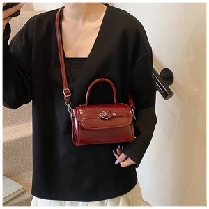 Detail of burgundy patent leather crossbody bag with metallic buckle on white stairs