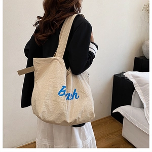Close-up of beige canvas tote bag with blue Bah print on black blazer outfit