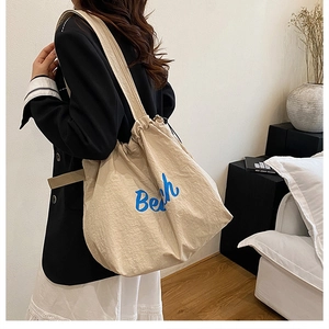 Close-up of beige canvas drawstring tote bag with blue Beach lettering on model shoulder