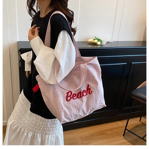 Close-up of pink canvas tote bag with red Beach lettering and stylish side ribbon detail