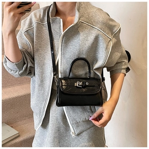 Detail of black patent leather crossbody bag with silver buckle worn with casual grey outfit